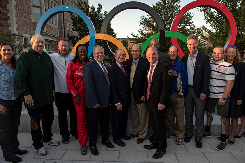 Olympic rings sculpture with people involved in the ceremony standing in front of it